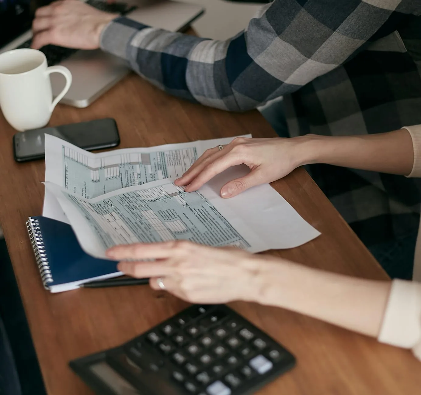Two people reviewing GST refund paperwork with a calculator on a desk